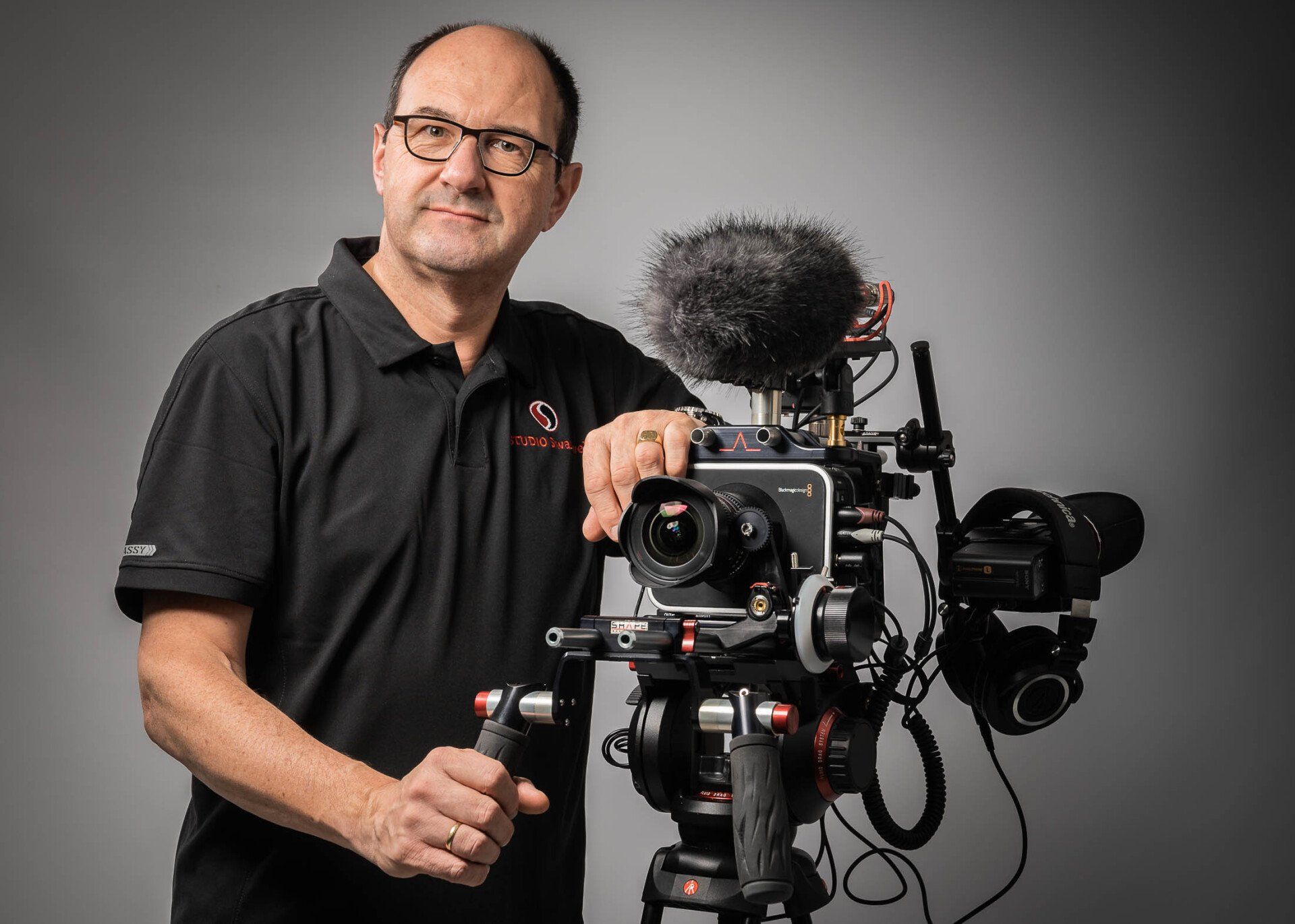 Een man in een zwart shirt houdt een camera op een statief vast.