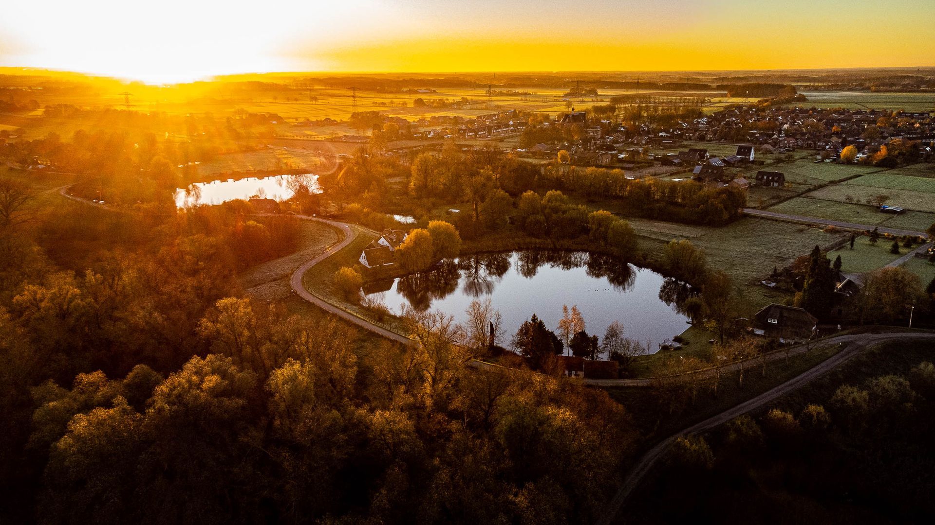 Een luchtfoto van een meer omgeven door bomen bij zonsondergang.