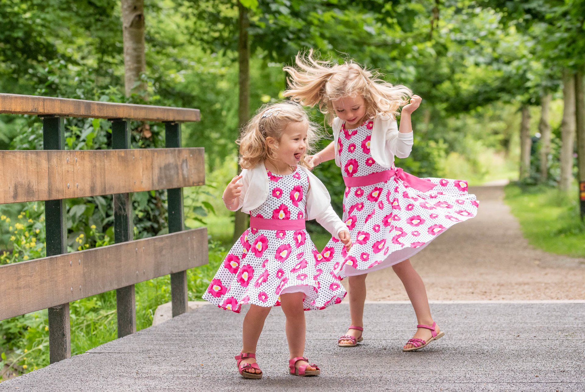 Twee kleine meisjes in roze jurkjes dansen op een brug.