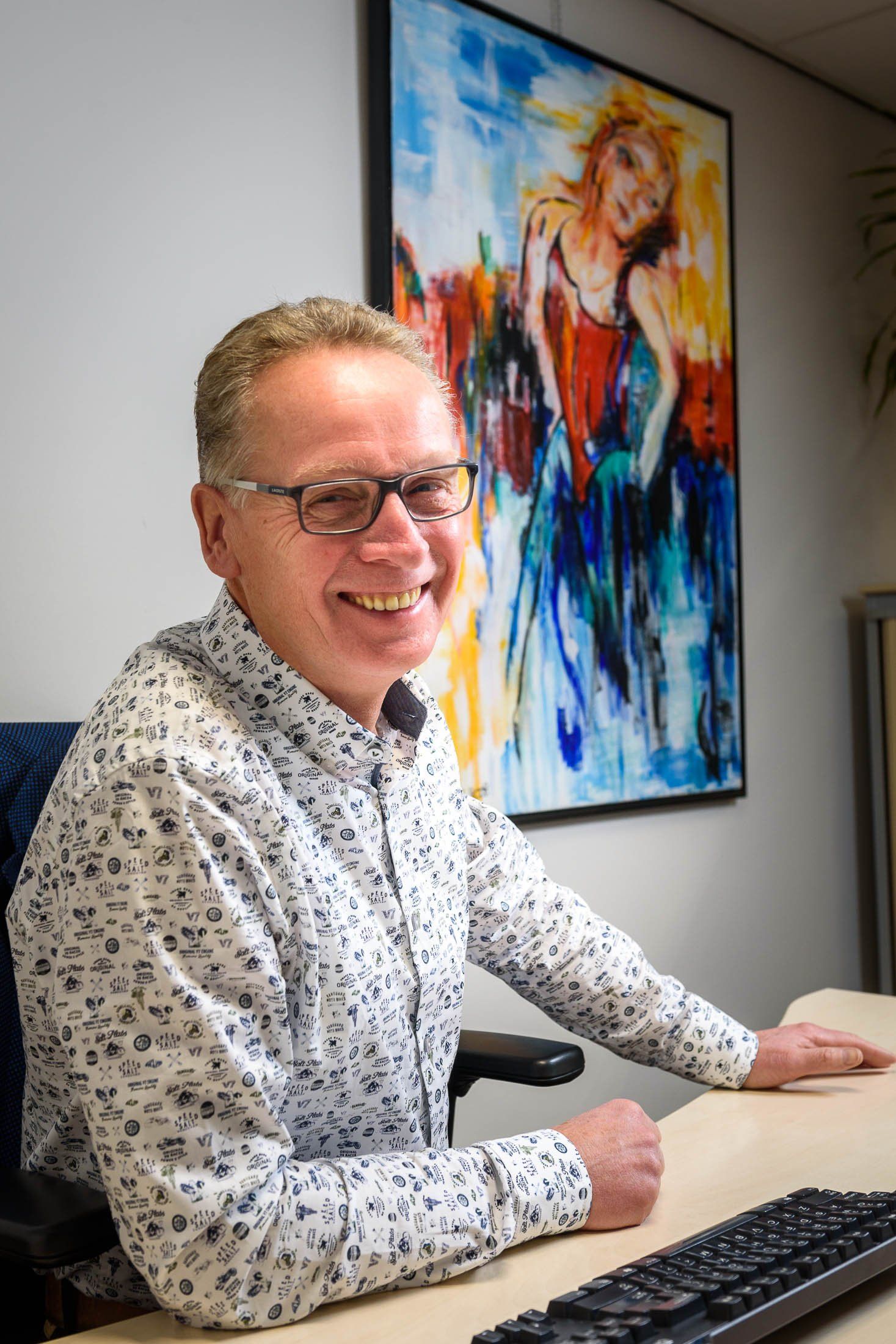 Een man zit aan een bureau met een computertoetsenbord voor een schilderij.