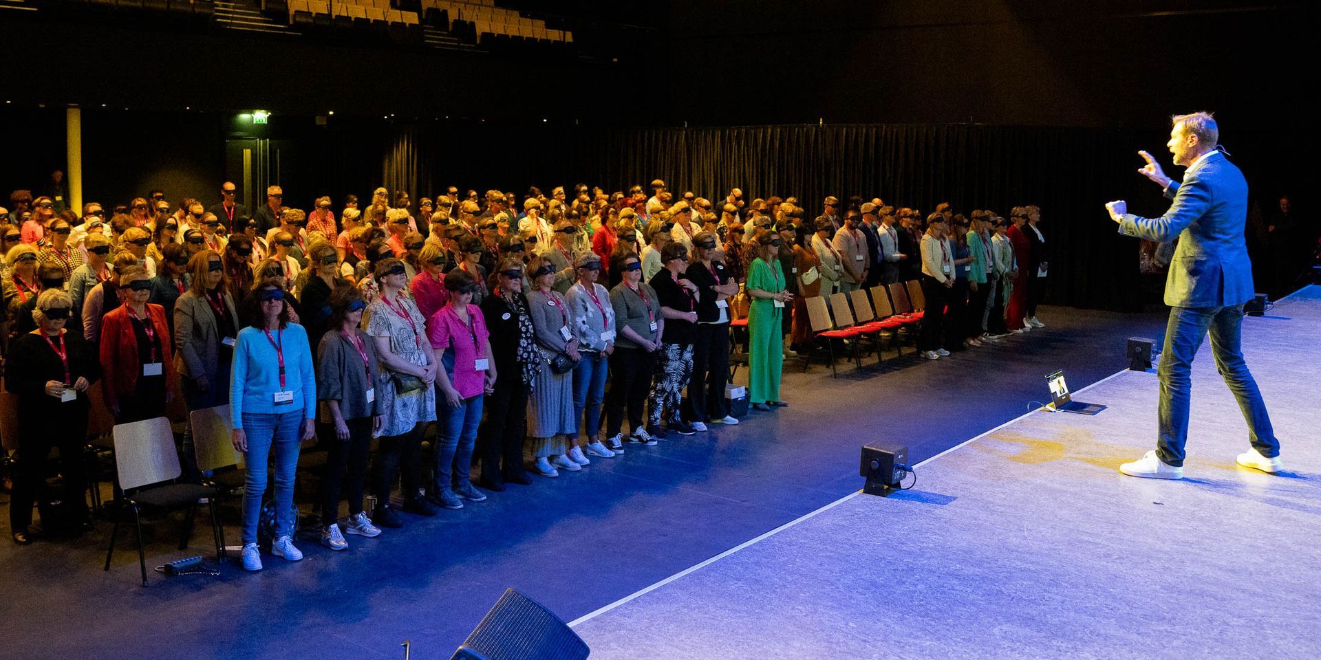Een man staat op een podium en geeft een presentatie aan een grote groep mensen.