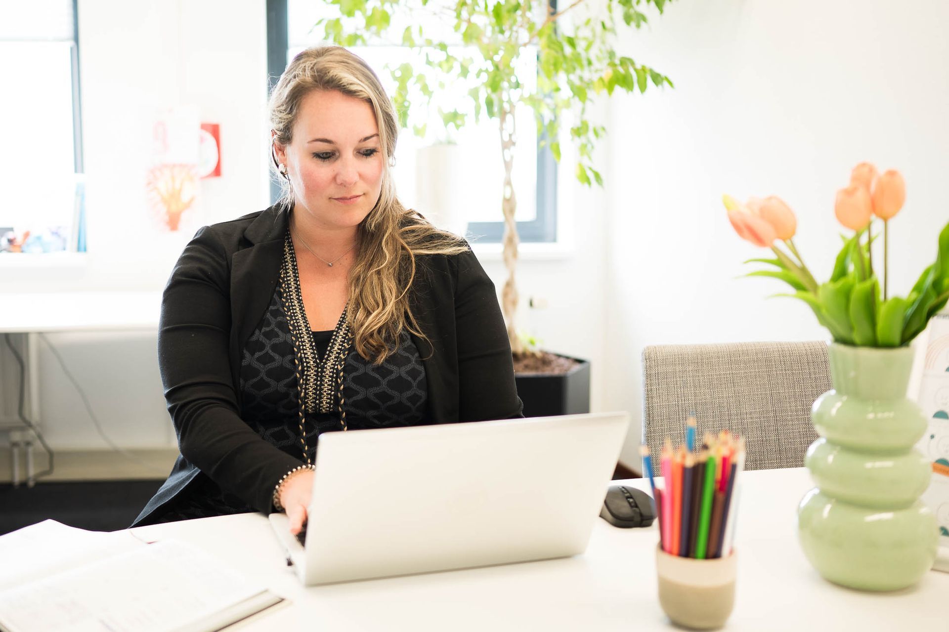 Een vrouw zit aan een bureau en gebruikt een laptop.