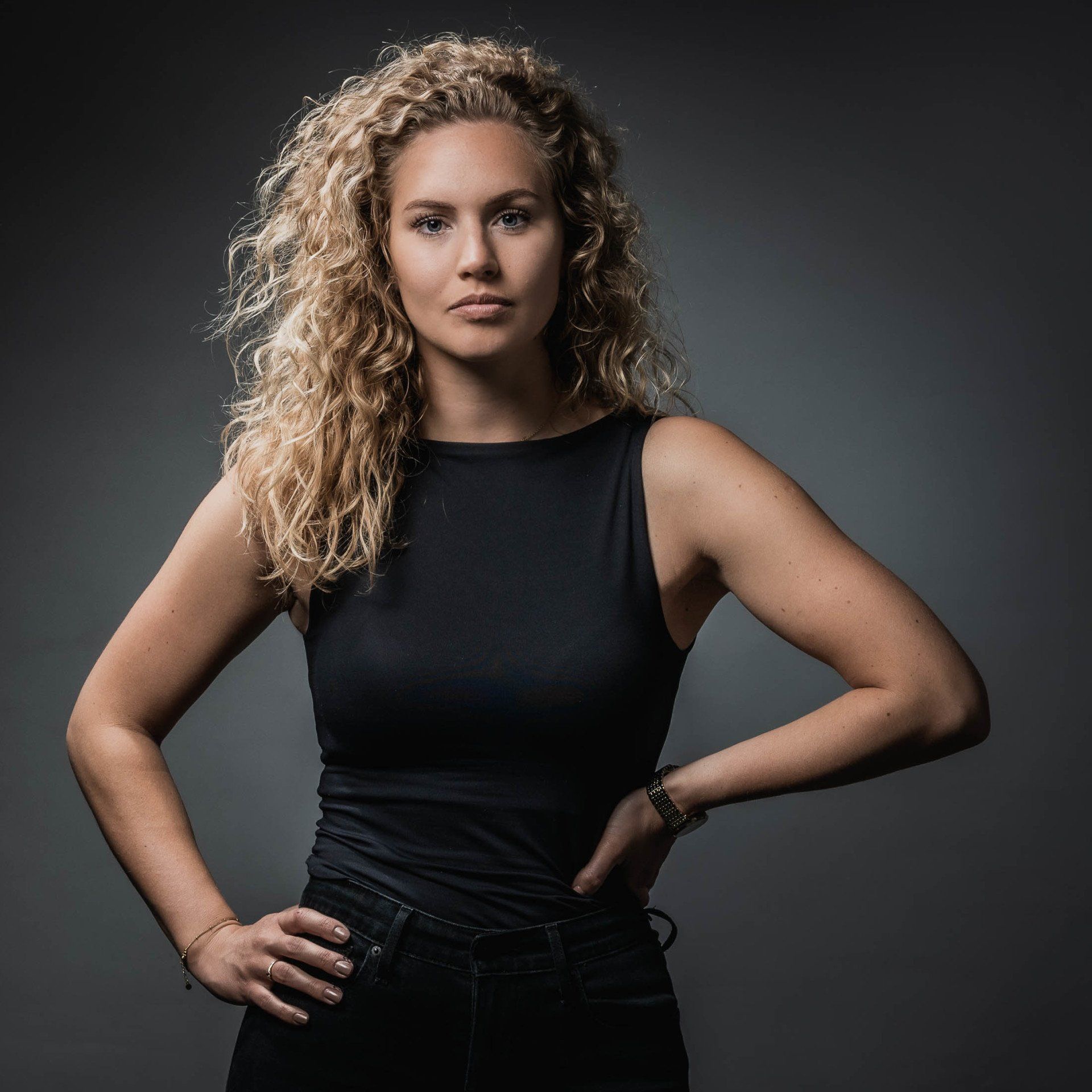 Een vrouw met krullend haar draagt een zwart tanktopje