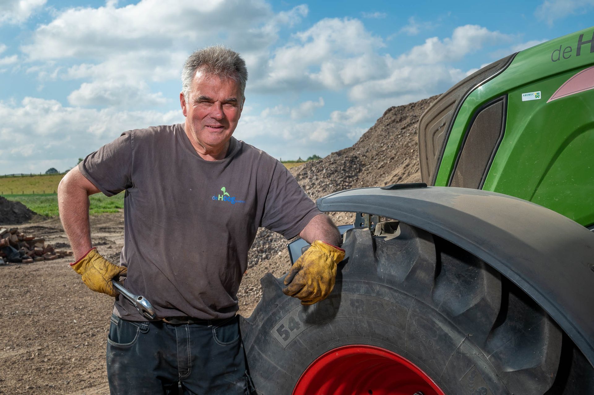 Een man staat naast een groene tractor met een moersleutel in zijn handen.