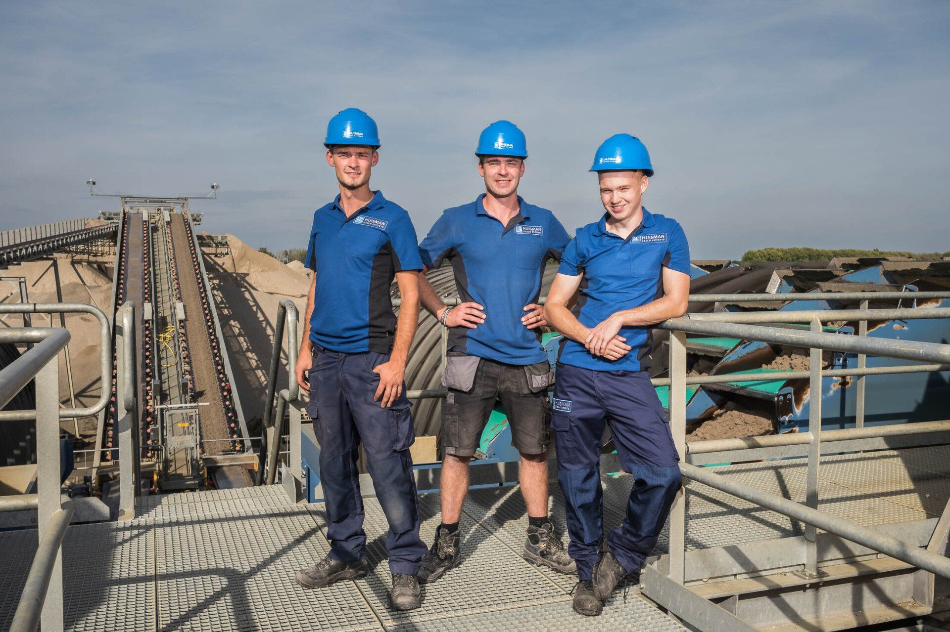 Drie mannen met helmen en blauwe shirts poseren voor een foto.