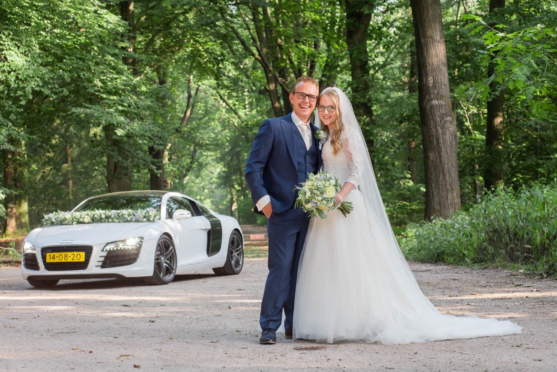 Een bruid en bruidegom poseren voor een foto voor een witte auto.