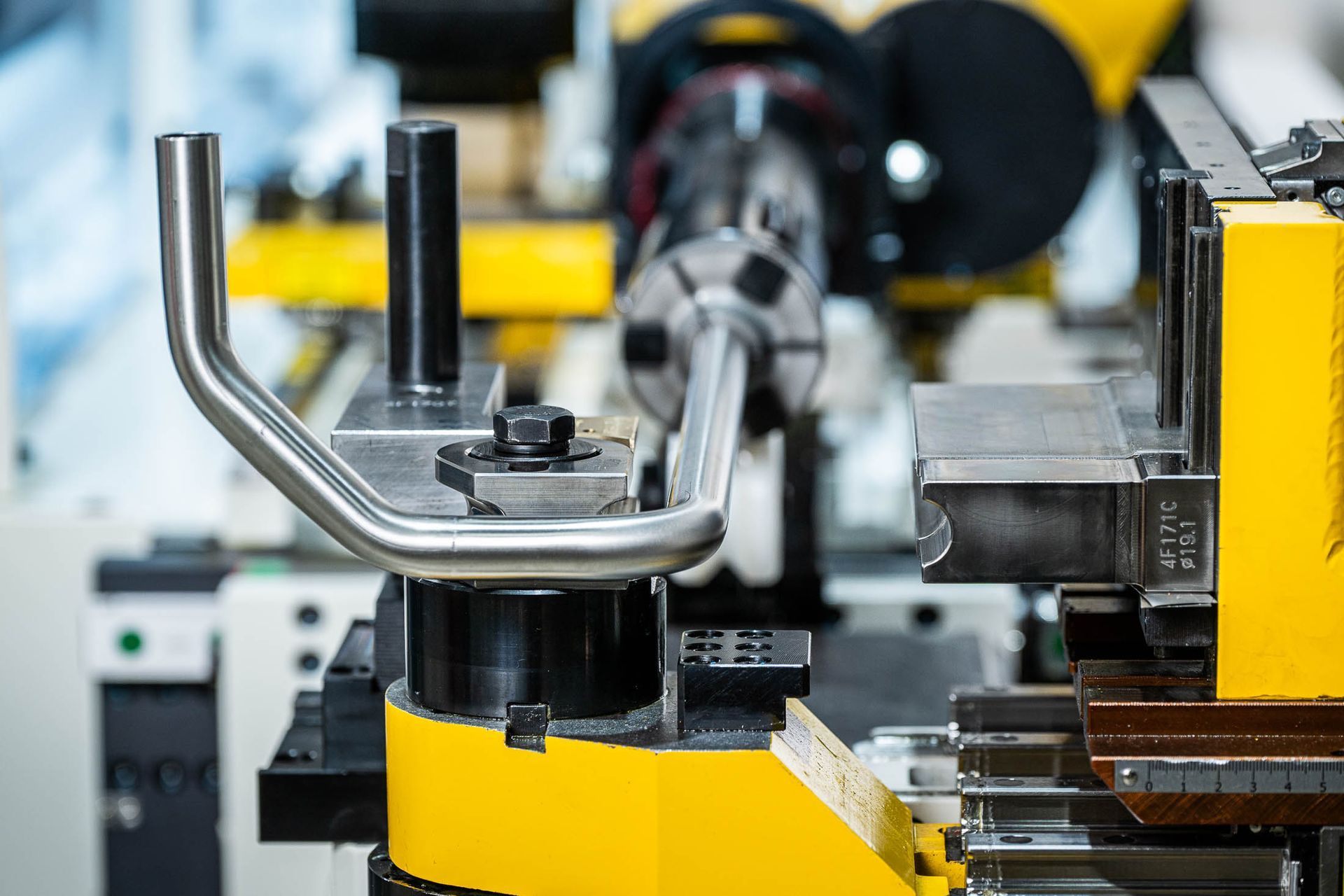 Close-up van een metaalbuigmachine waarop een gebogen metalen handgreep wordt gevormd. Gele en zwarte details van de machine.