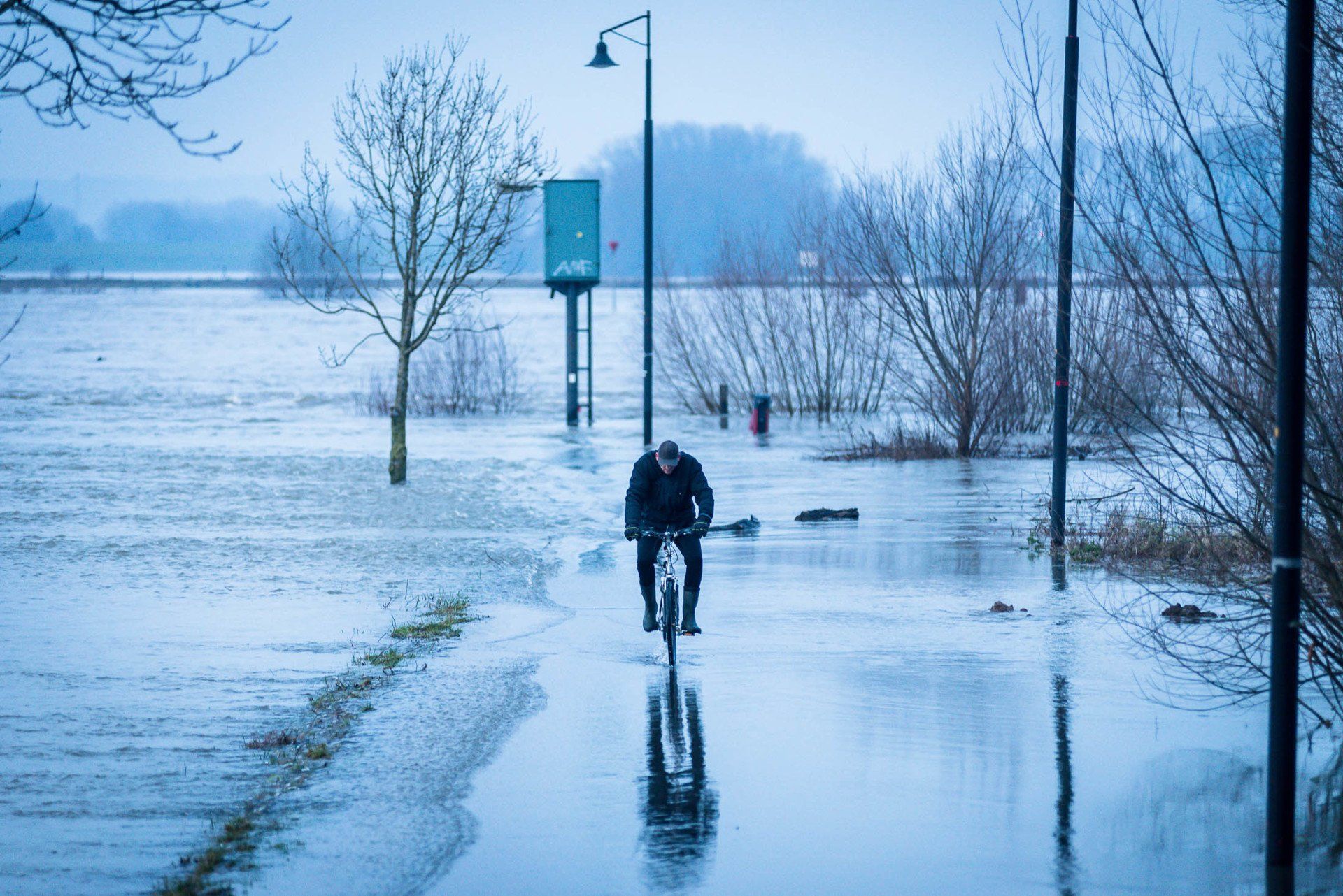 Een man fietst op een overstroomde weg.