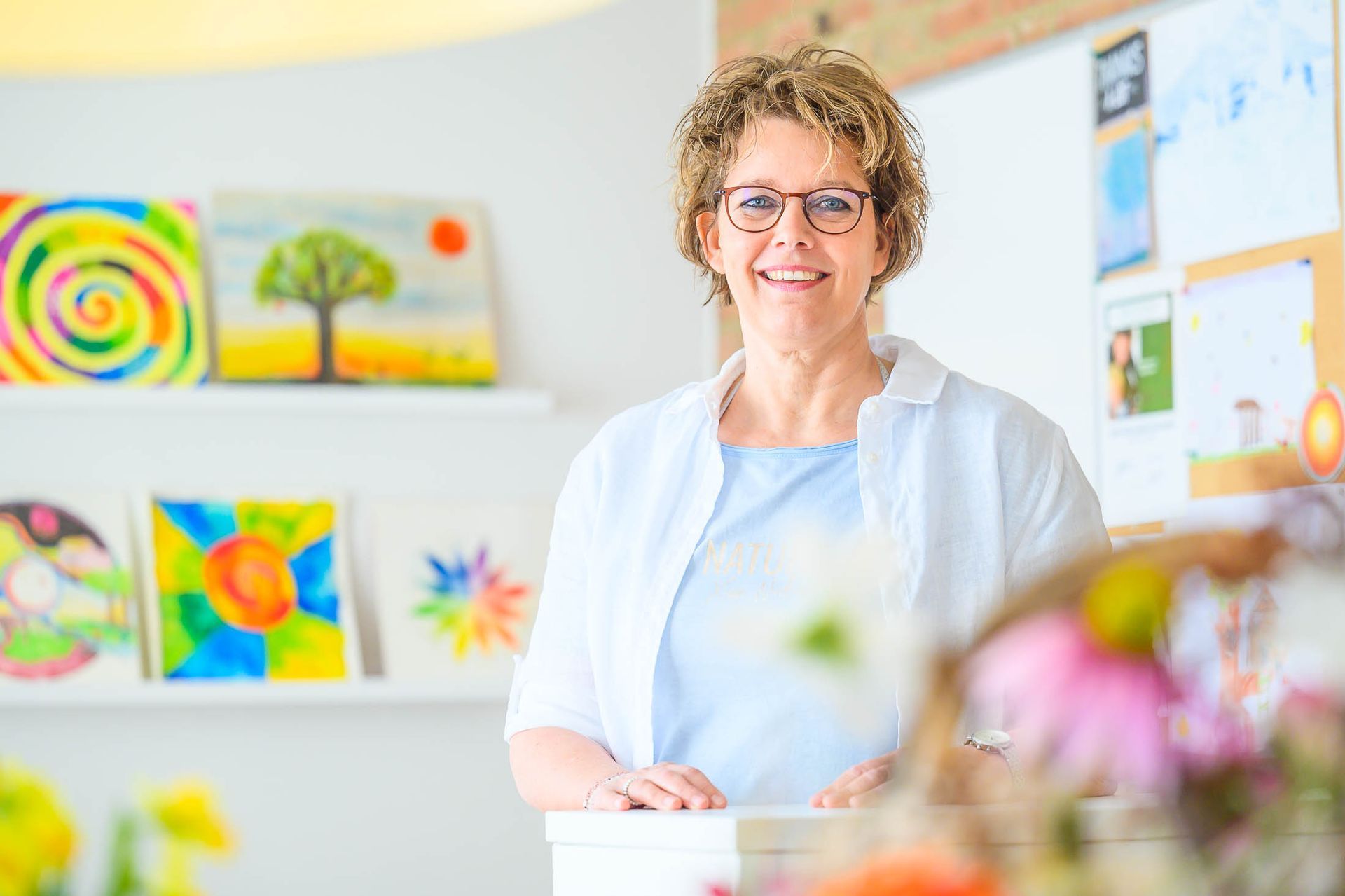 Een vrouw staat voor een tafel in een kamer met schilderijen aan de muur.