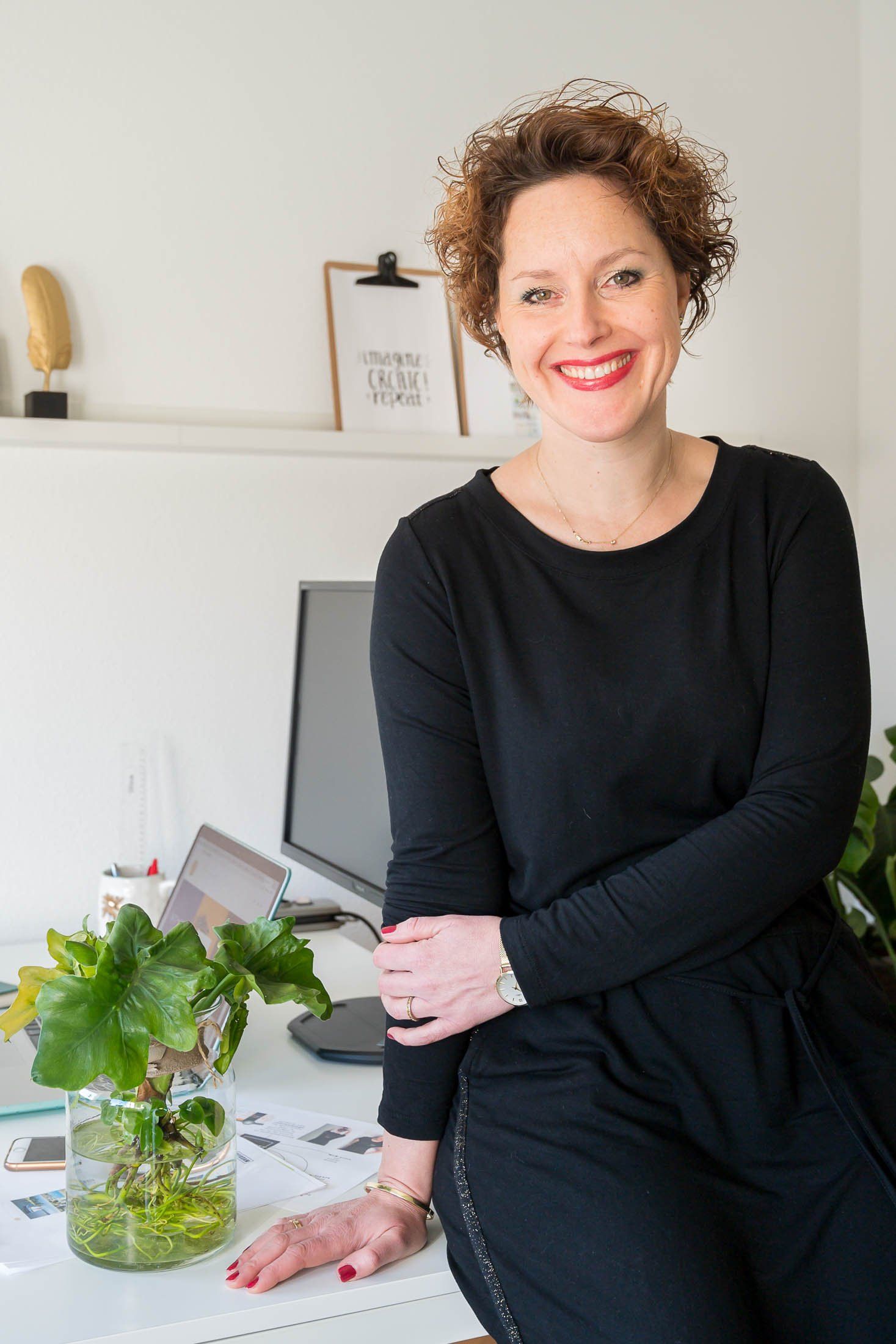 Een vrouw in een zwart shirt zit aan een bureau met haar armen over elkaar.