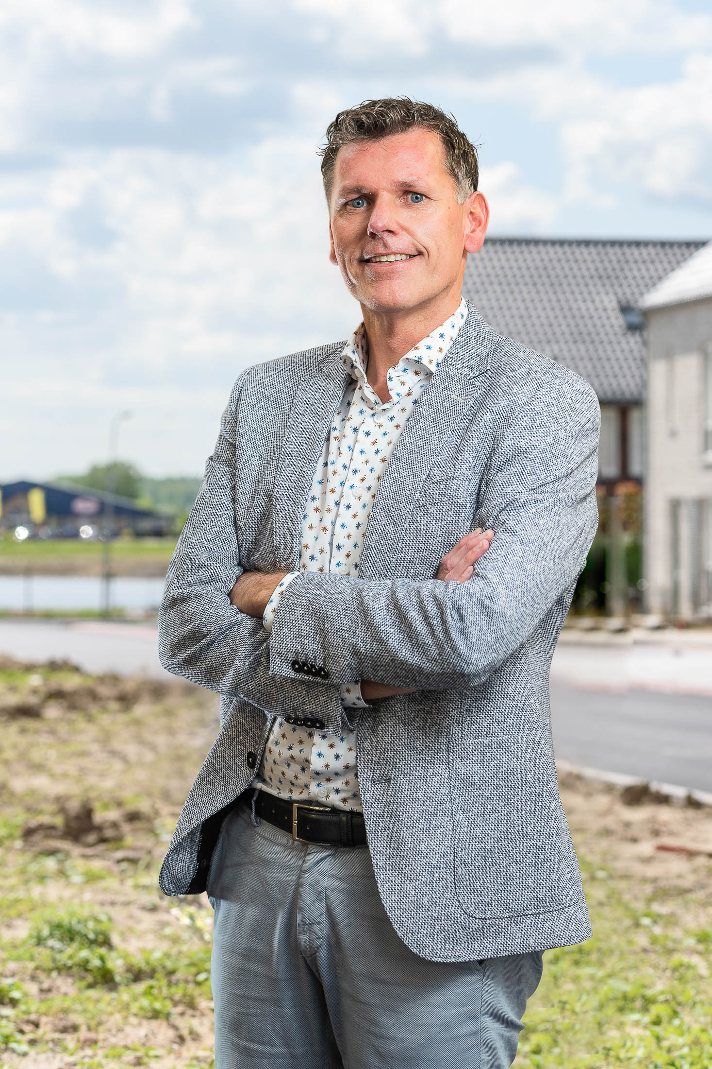 Een man in pak staat in een veld met zijn armen over elkaar.