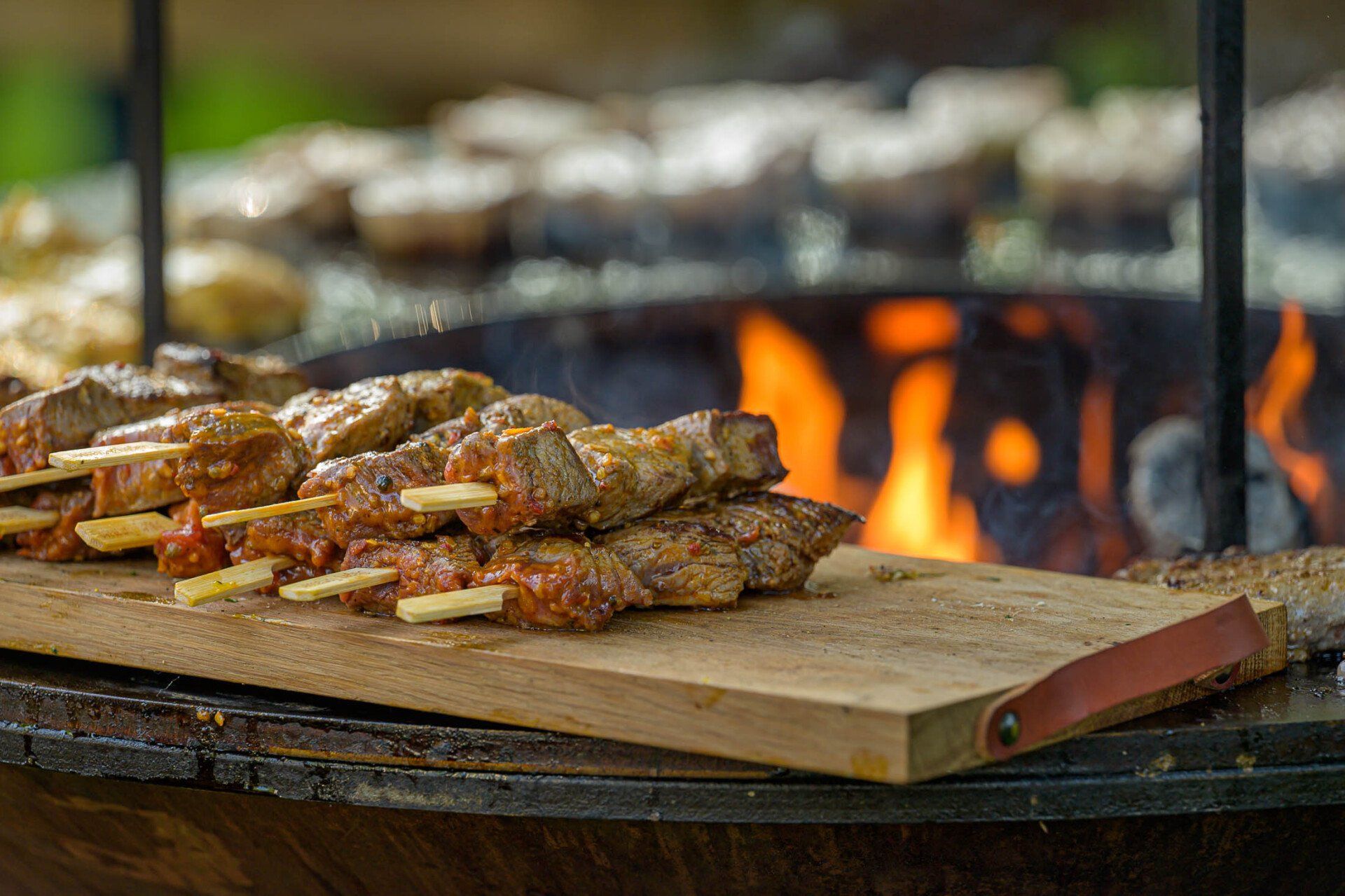Een houten snijplank met vleesstokjes erop voor een vuur.