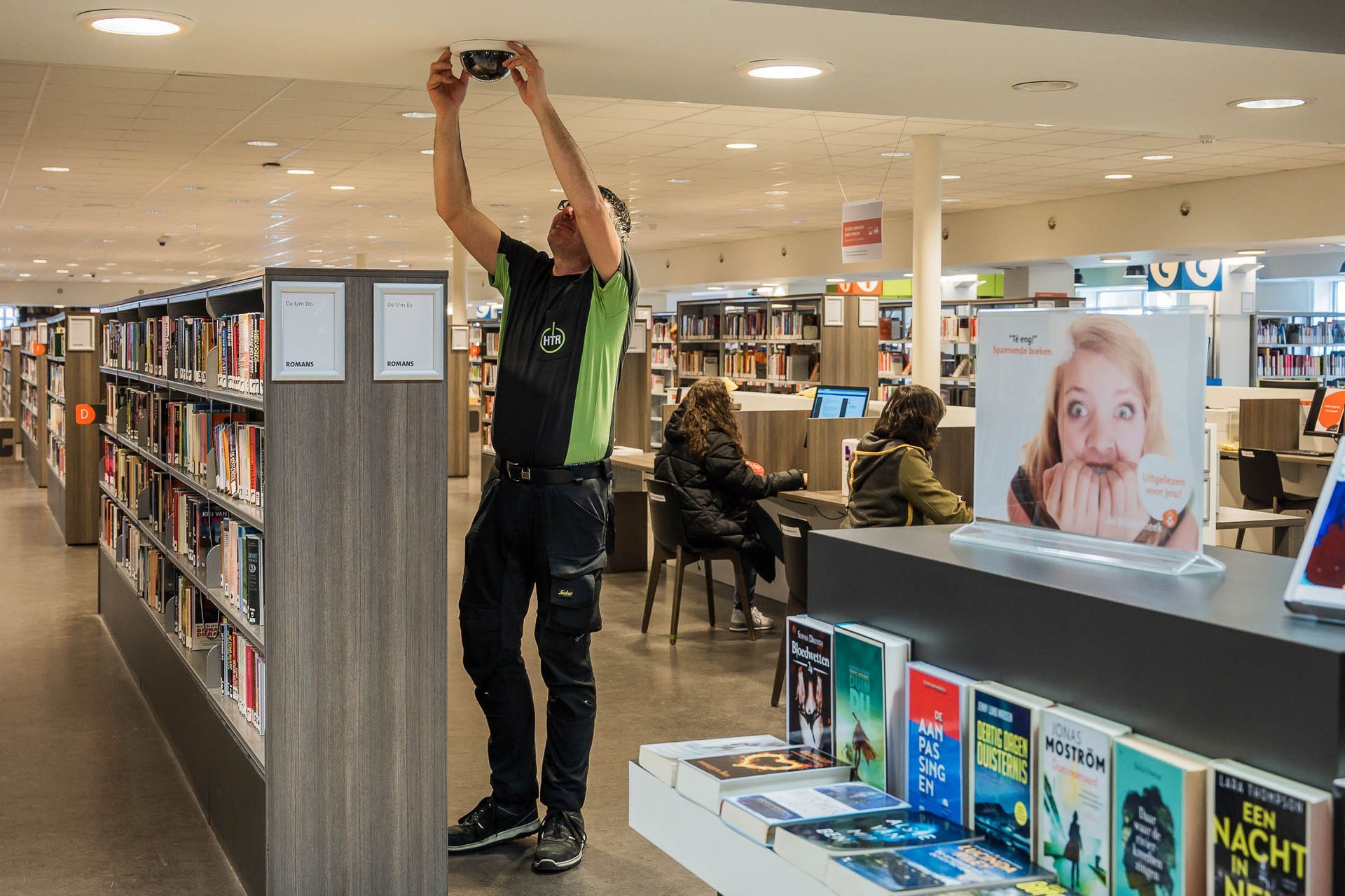 Een man werkt aan een brandalarm in een bibliotheek.