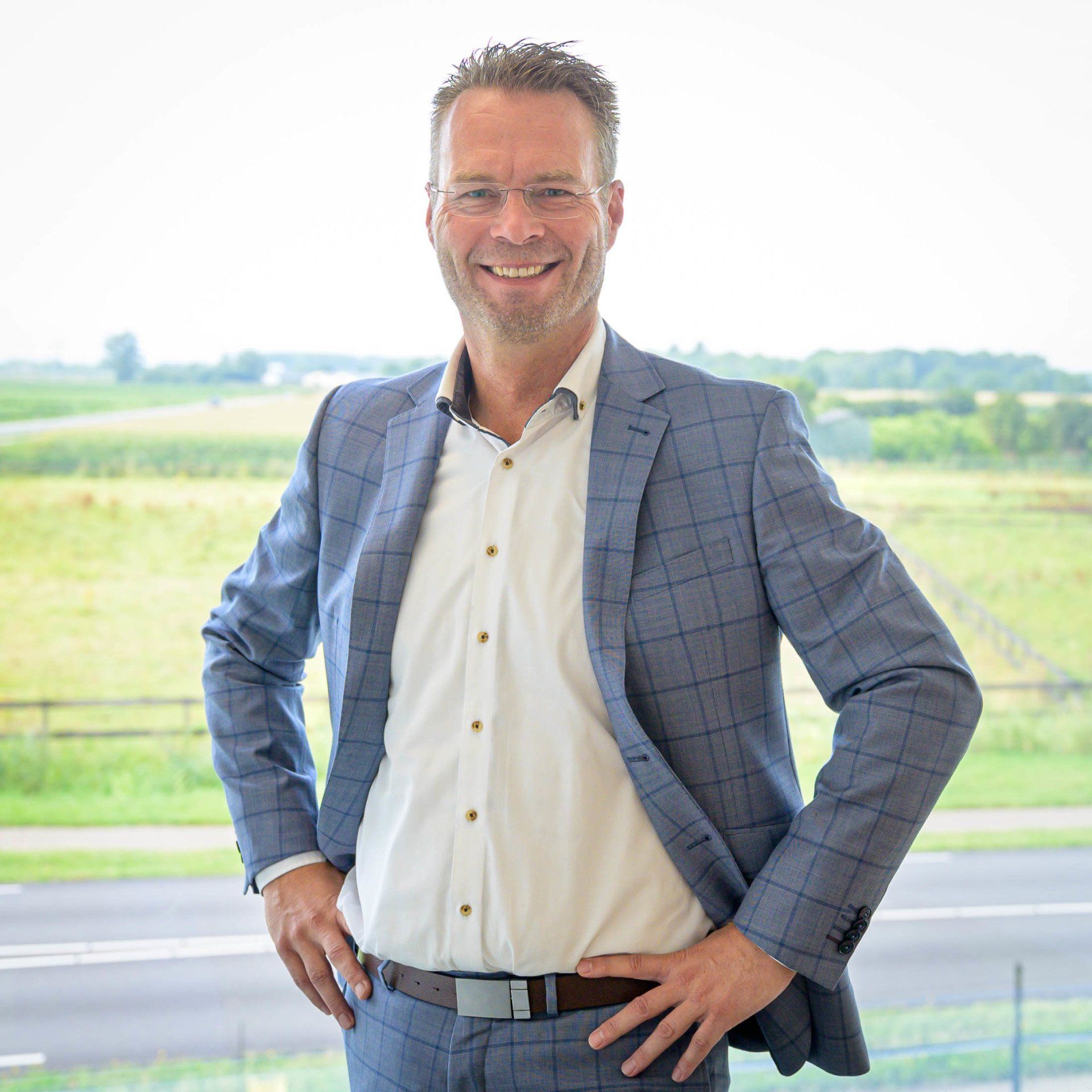 Een man in een pak en een wit overhemd staat met zijn handen in zijn zij.