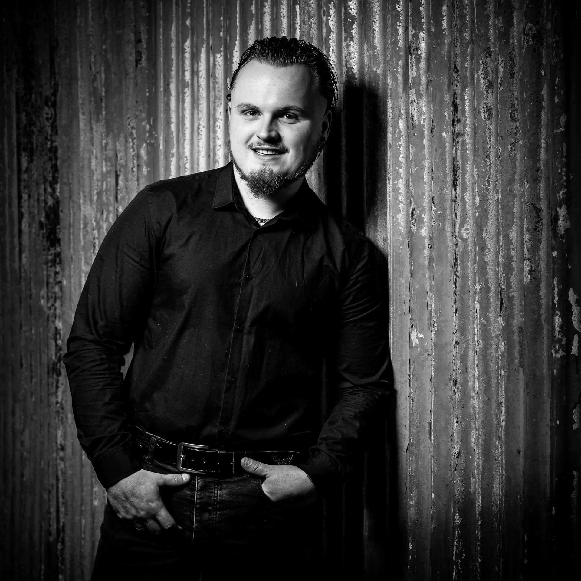 Een man in een zwart shirt staat voor een metalen wand.