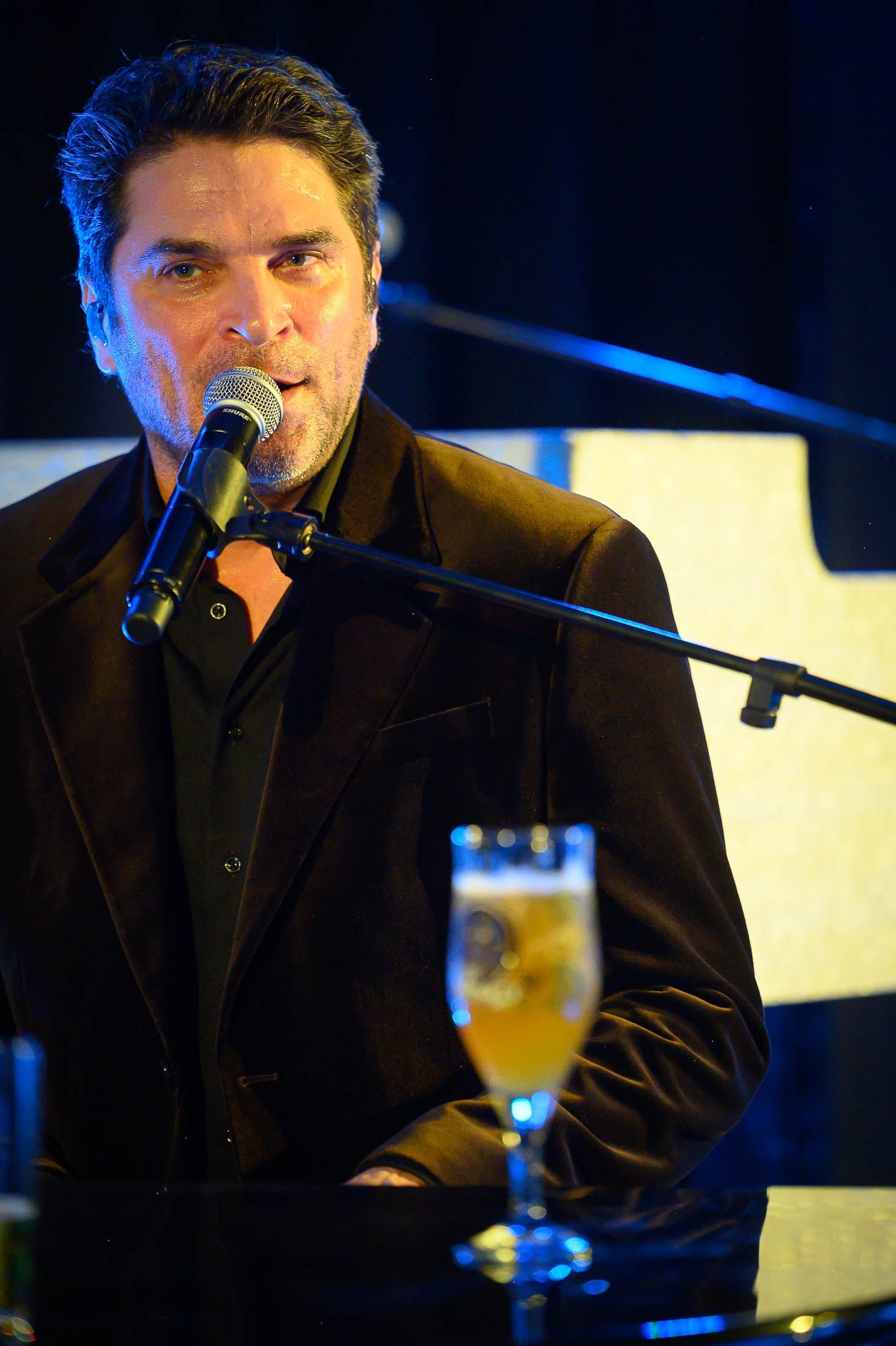 Een man zingt in een microfoon naast een glas bier.