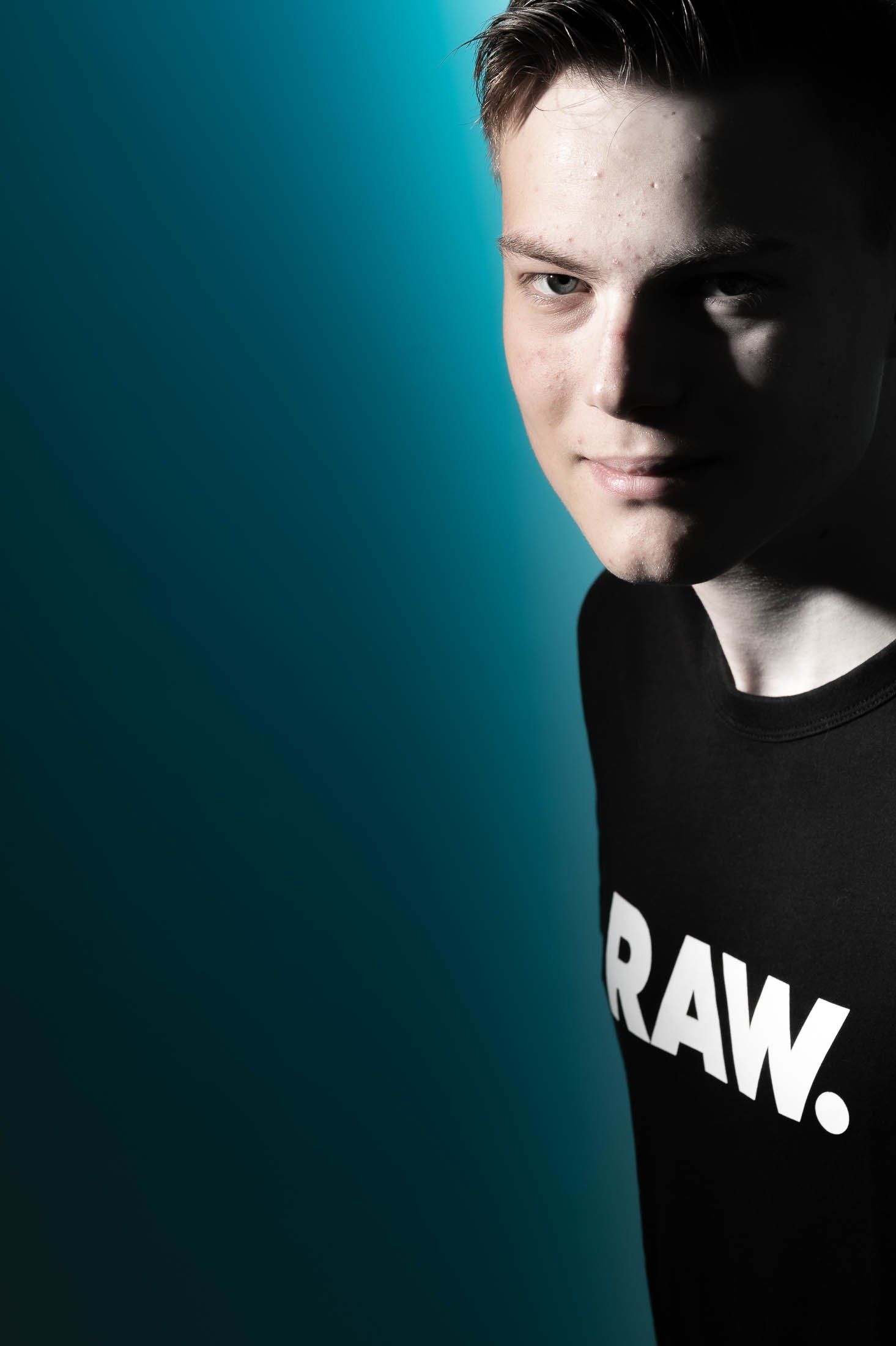 Een jongeman in een zwart shirt met de tekst raw