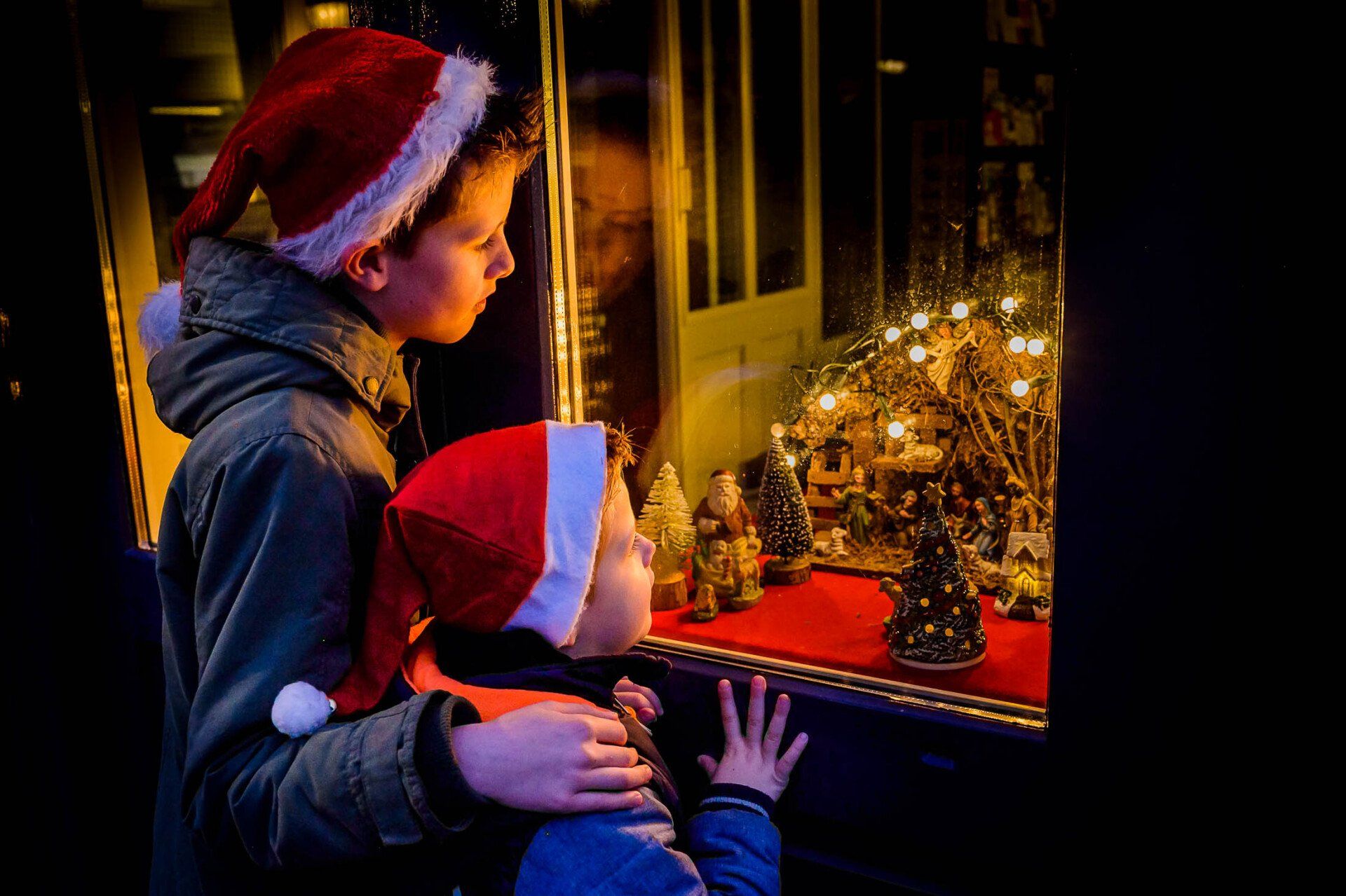 Twee jongetjes met kerstmutsen kijken naar een kerstetalage.