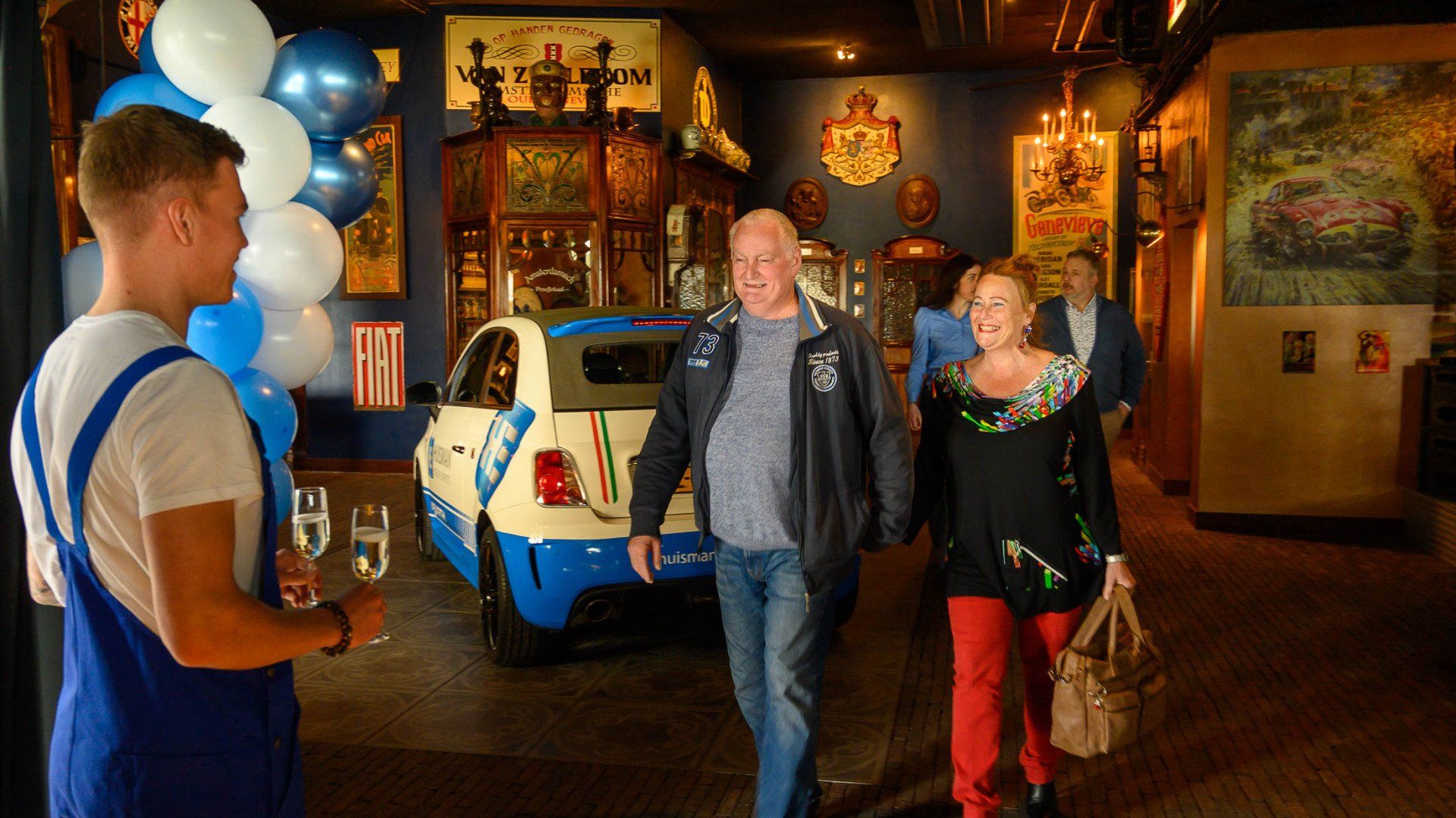 Een man en een vrouw lopen voor een blauw-witte auto.