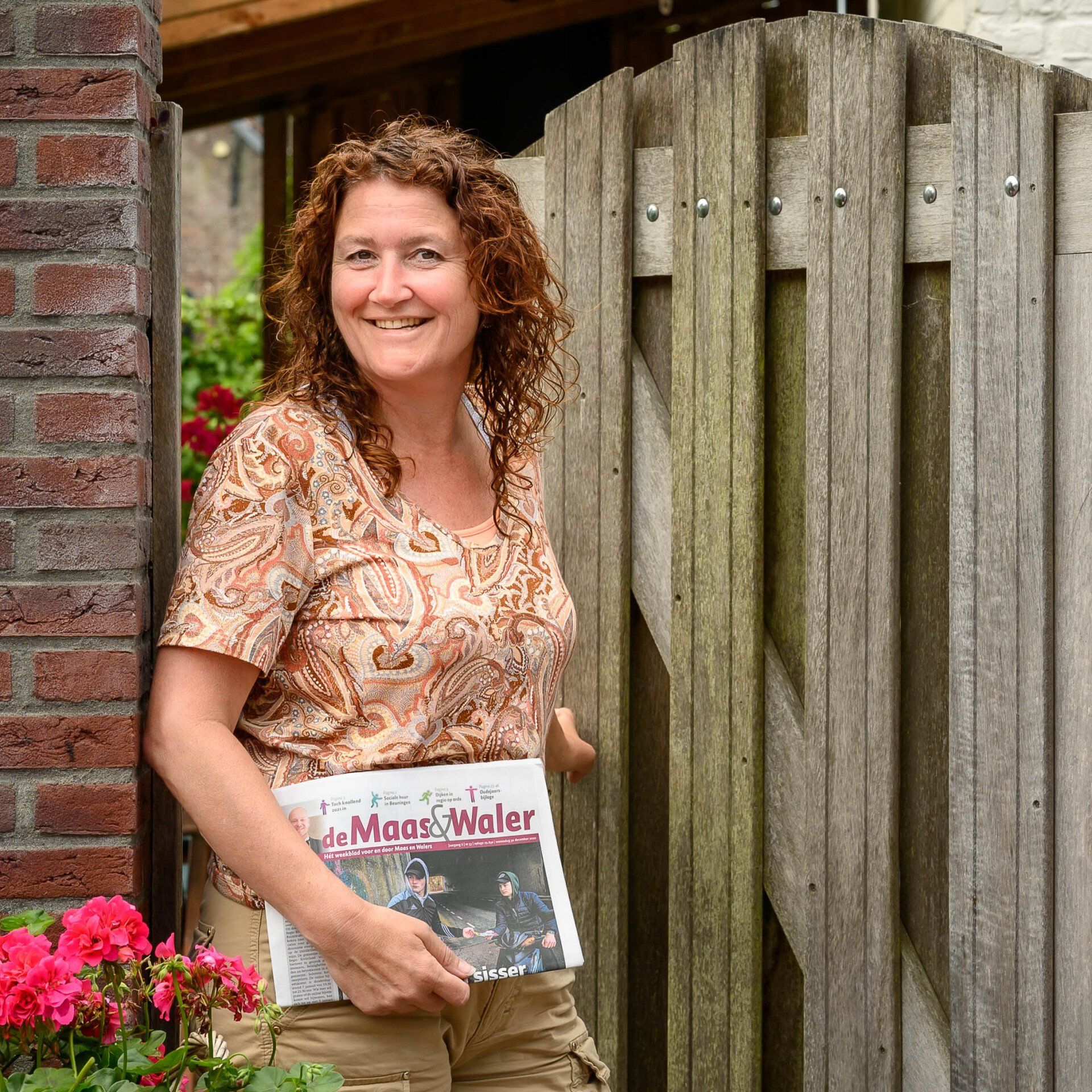 Een vrouw die voor een houten hek staat en een tijdschrift vasthoudt met de tekst 'mooi water' erop