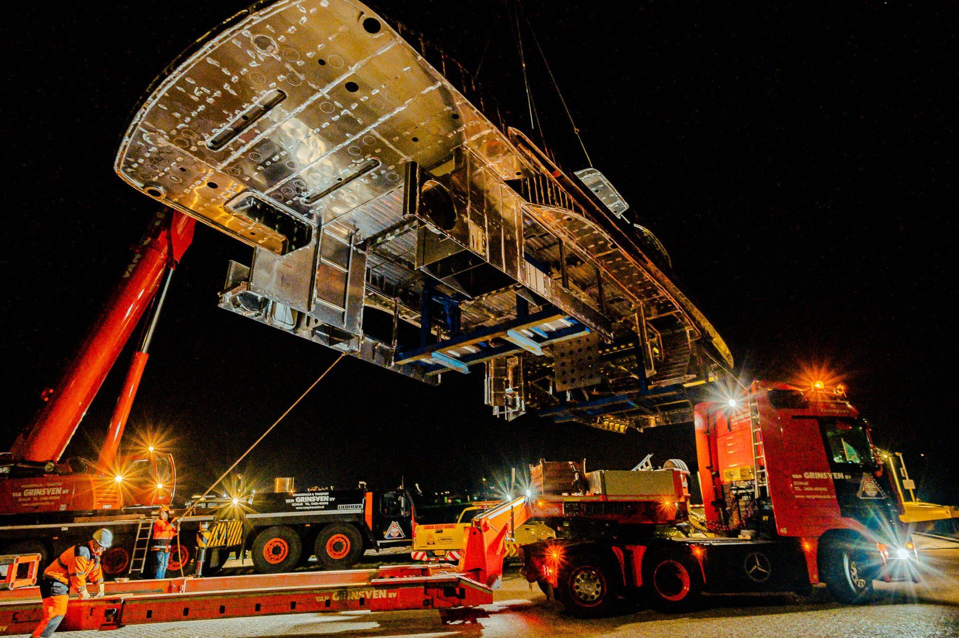 Een groot stuk metaal wordt door een kraan de lucht in gehesen.