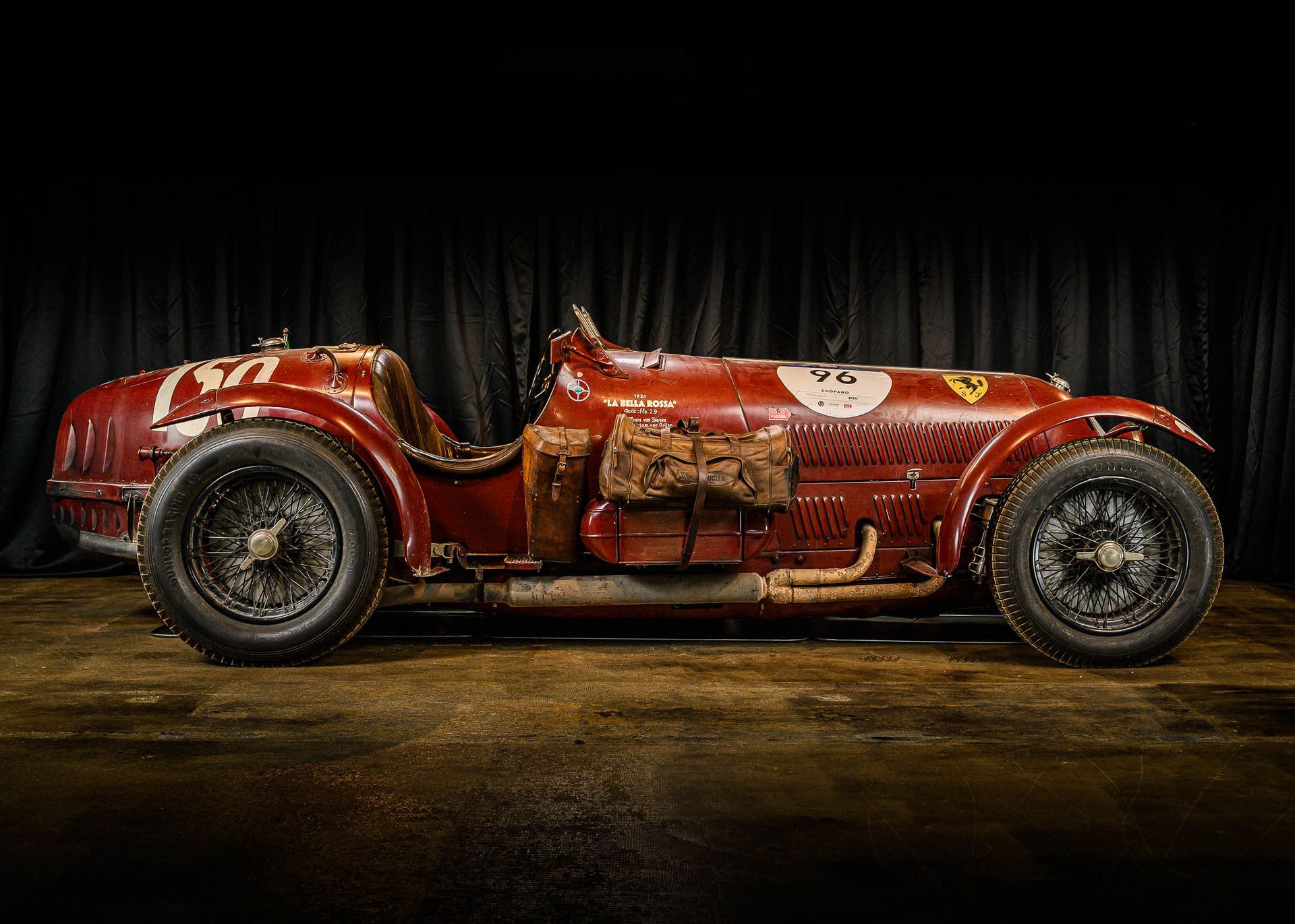 Een rode raceauto staat geparkeerd voor een zwart gordijn in een garage.