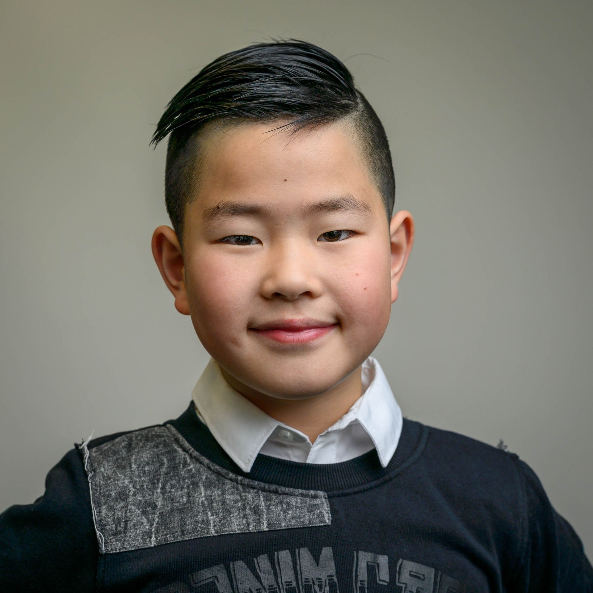 Een jonge jongen draagt een zwarte trui en een wit overhemd.