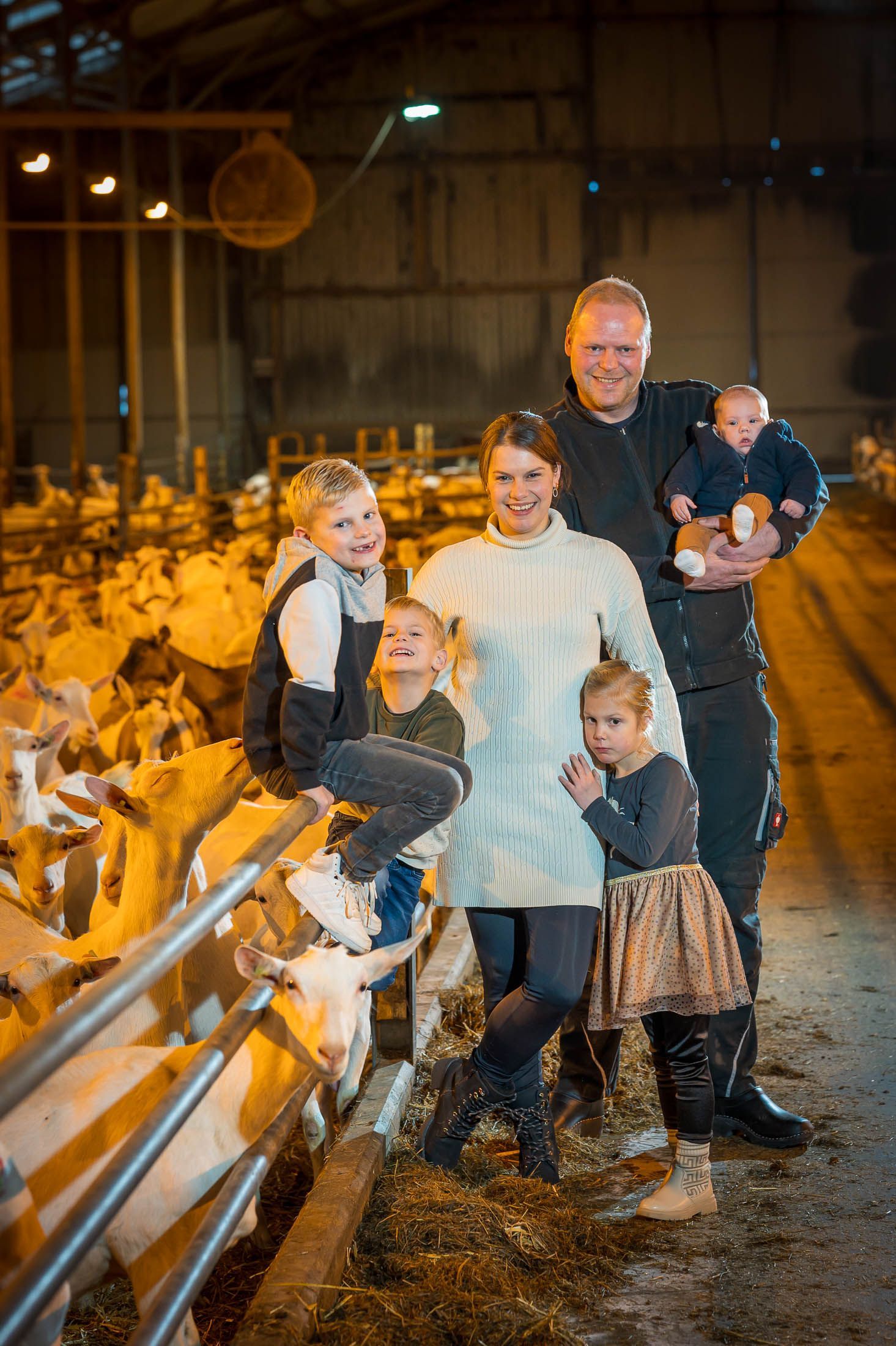 Een gezin poseert voor een foto in een schuur met geiten.