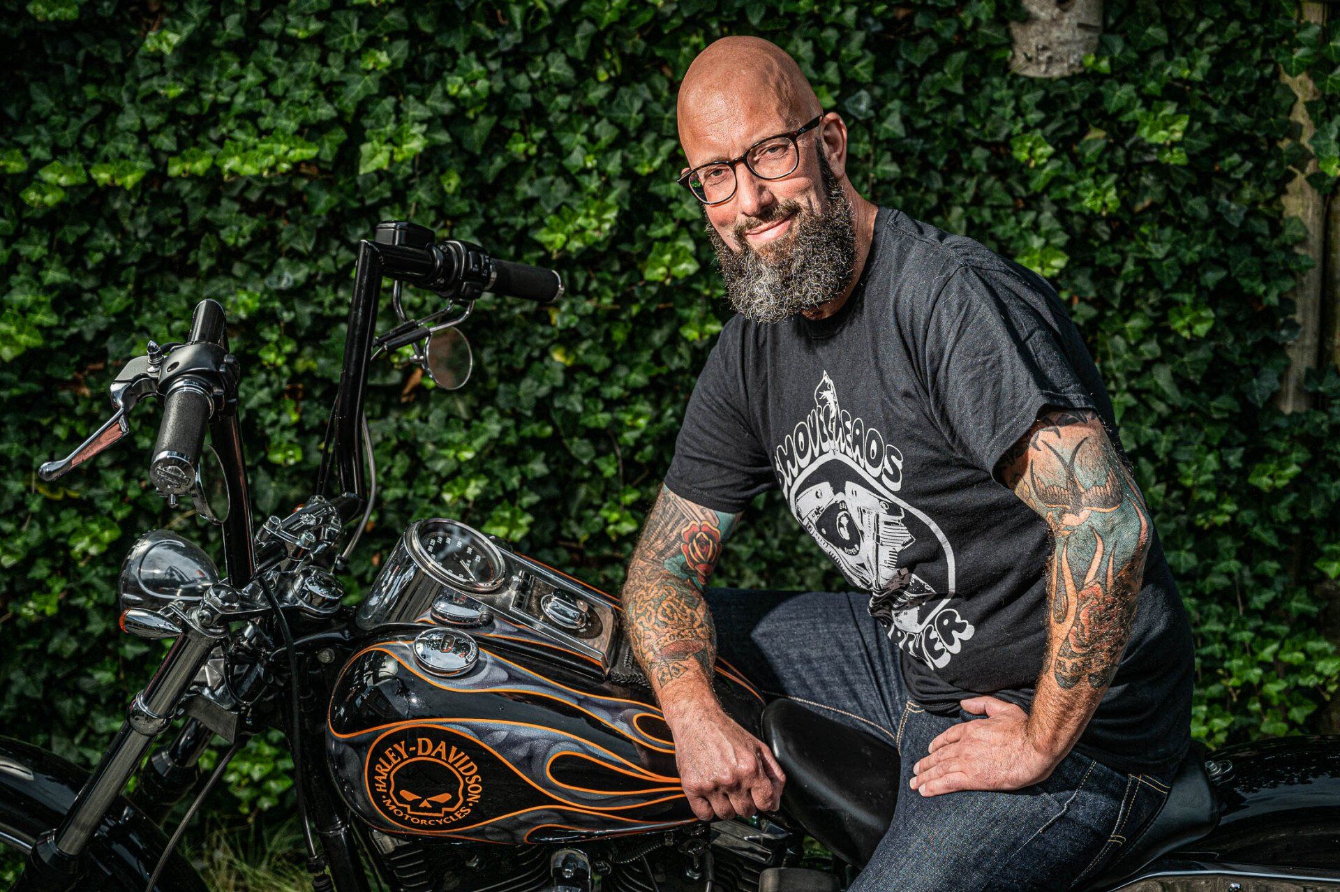 Een man met een baard en tatoeages zit op een motorfiets.