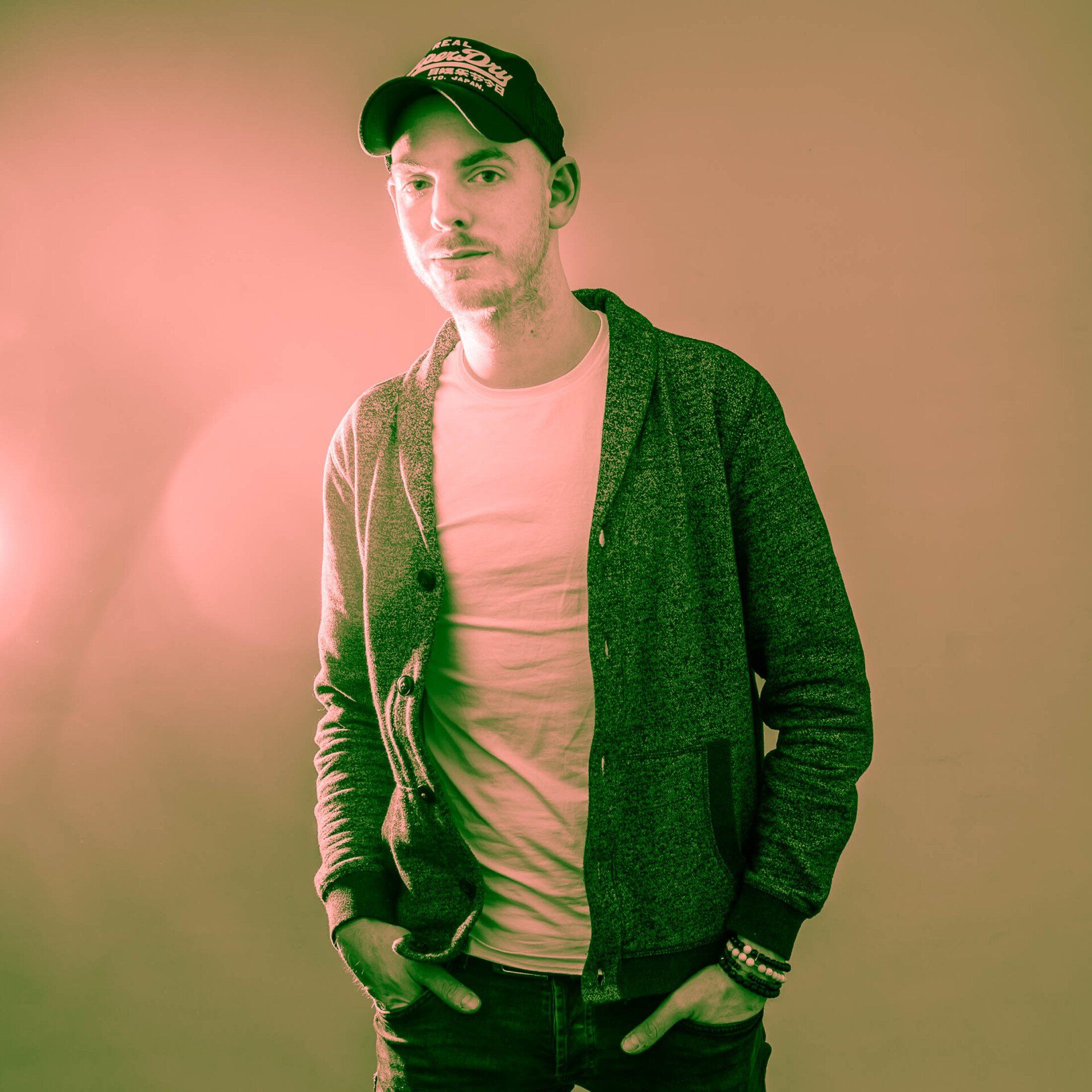 Een man met een hoed en een jas staat met zijn handen in zijn zakken.