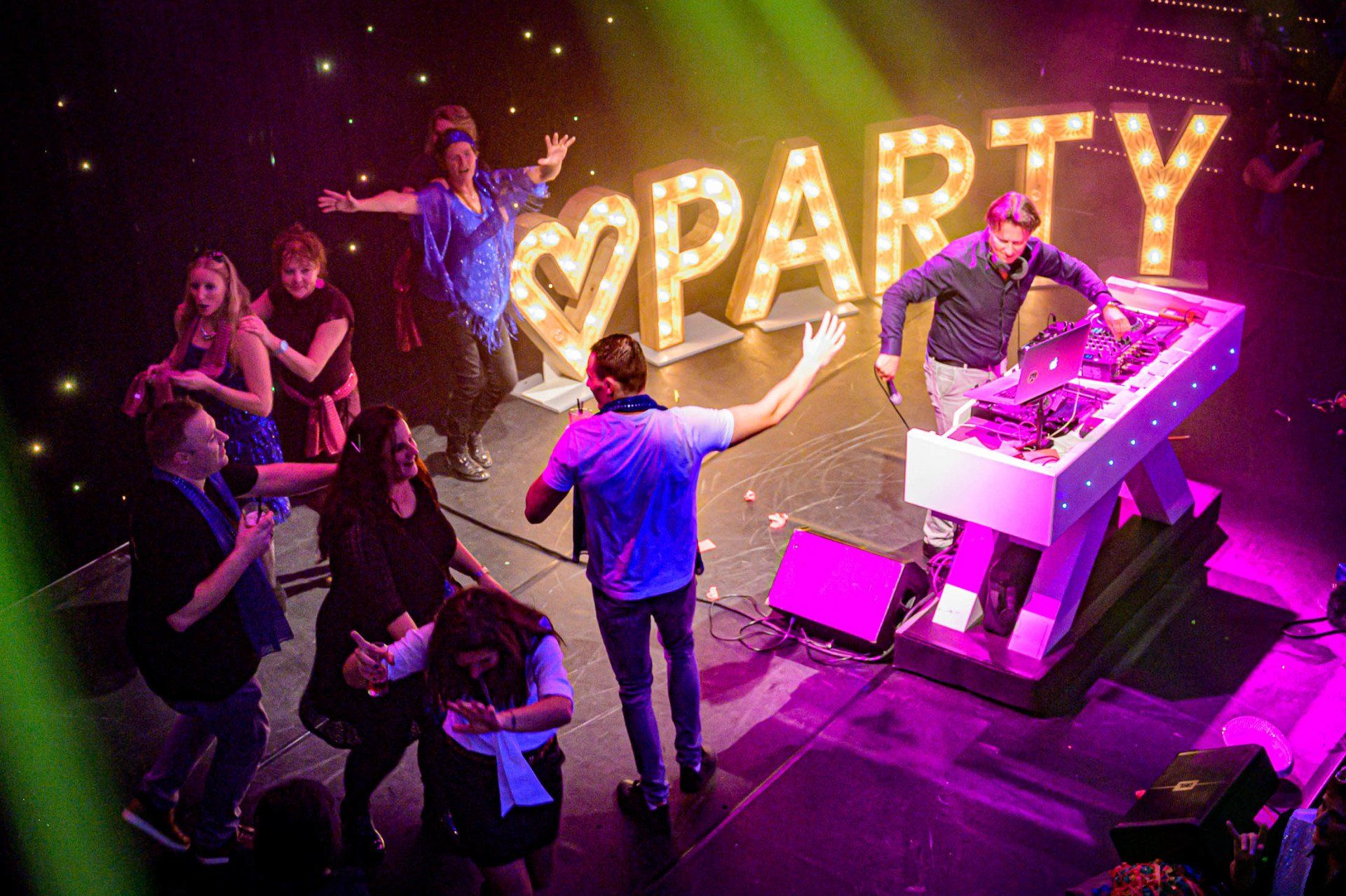 Een groep mensen danst voor een bord waarop 'feest' staat.