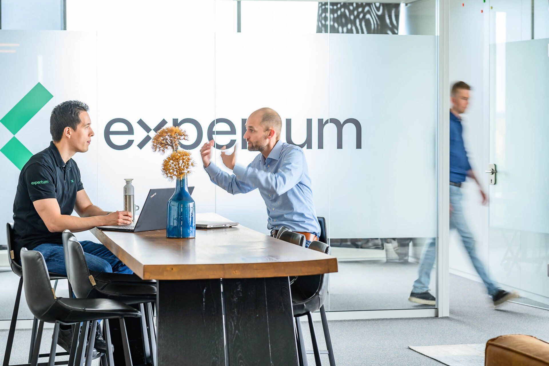 Twee mannen zitten aan een tafel voor een bordje met het opschrift 'experium'.