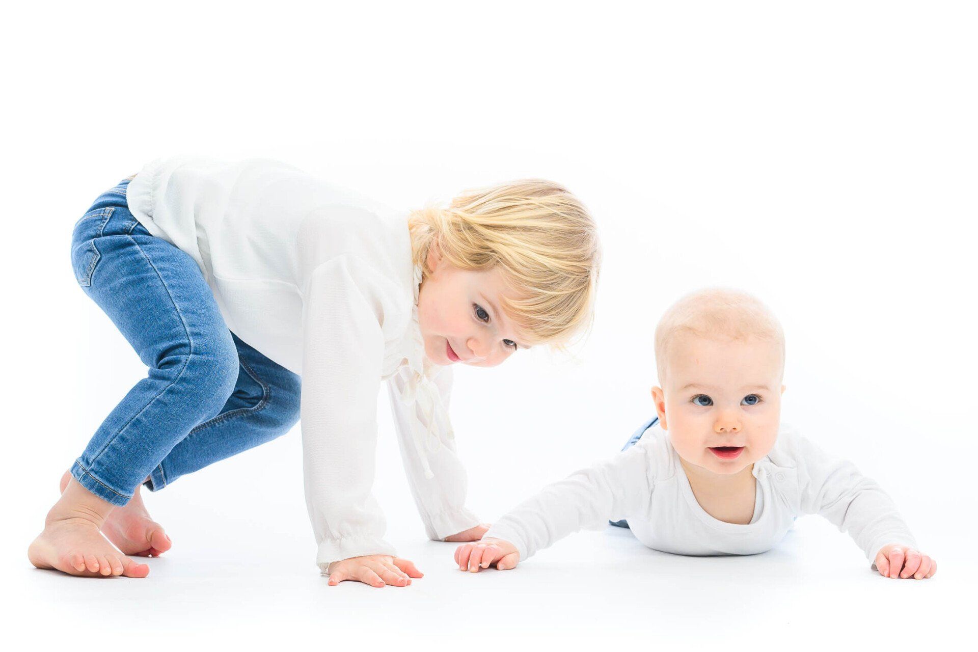 Een klein meisje kruipt naast een baby op de grond.