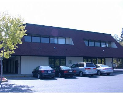 Building with dark roof, windows, and parked cars in front.