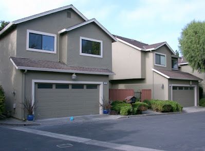 Row of two-story townhouses with gray siding, garages, and small front yards.
