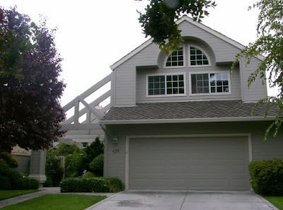 Two-story house with gray garage door, white-framed windows, and an arch window; with trees and green grass.