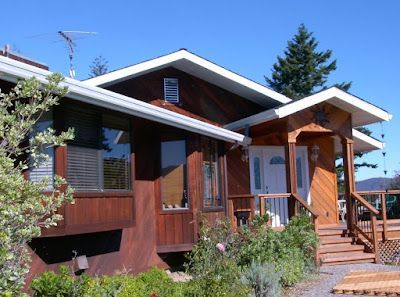 Brown wooden house with white trim, porch, and steps; sunny day.
