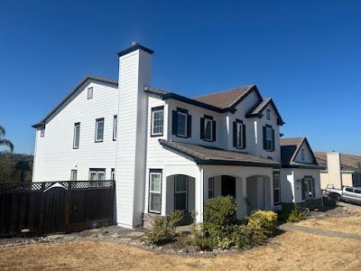 White house with black shutters, brown roof, and chimney against a blue sky.