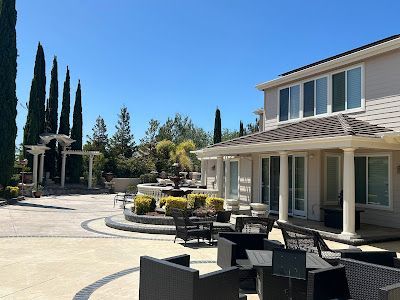 Backyard patio with seating, fountain, and multi-story house under a clear blue sky.