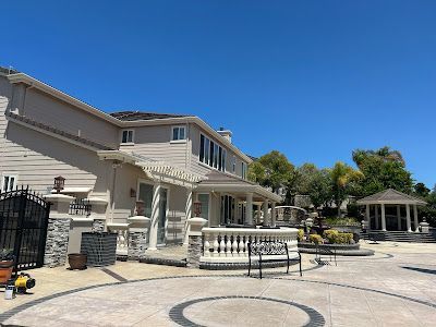 Two-story beige house with stone accents and a gazebo on a sunny day.