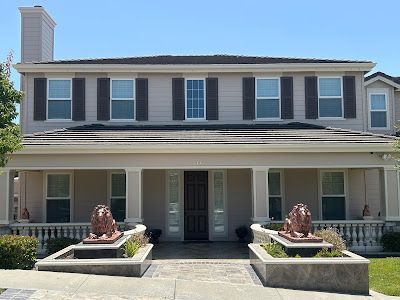 Two-story beige house with brown shutters and columns. Two lion statues flank the front door.