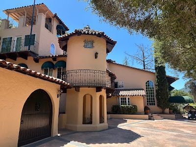 Mediterranean-style mansion with a tower and balcony, beige walls, blue sky, and trees in the background.