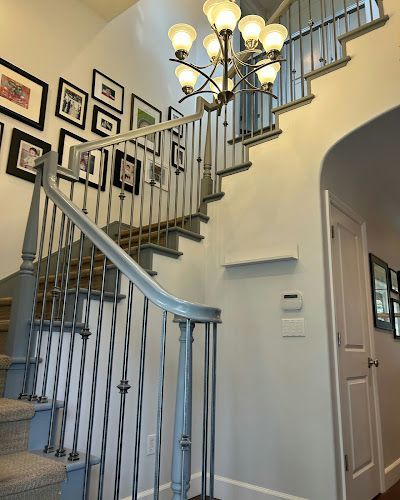Staircase with blue banister and gray steps, leading up to a light fixture and framed photos on the wall.