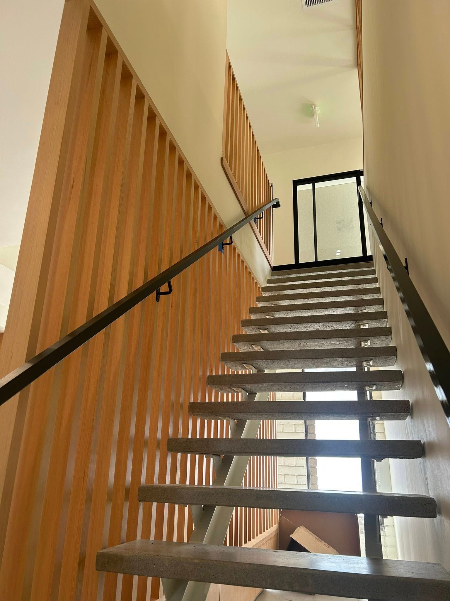 Staircase with wooden slatted wall and black handrail. Door at top.