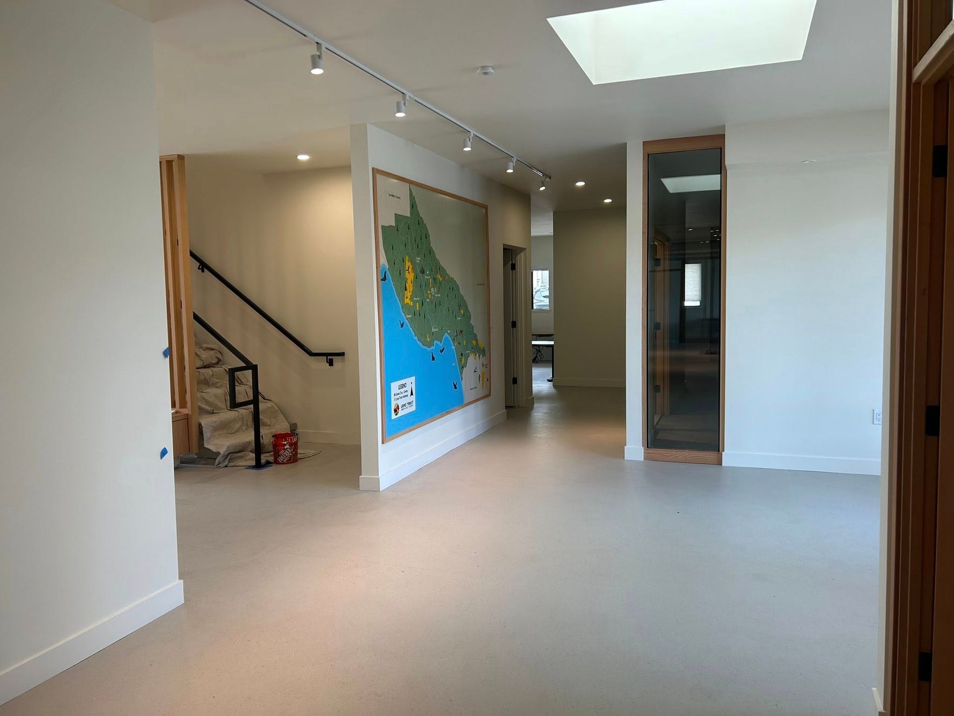 Empty, light-filled hallway with map on the wall, skylight, staircase, and glass door.