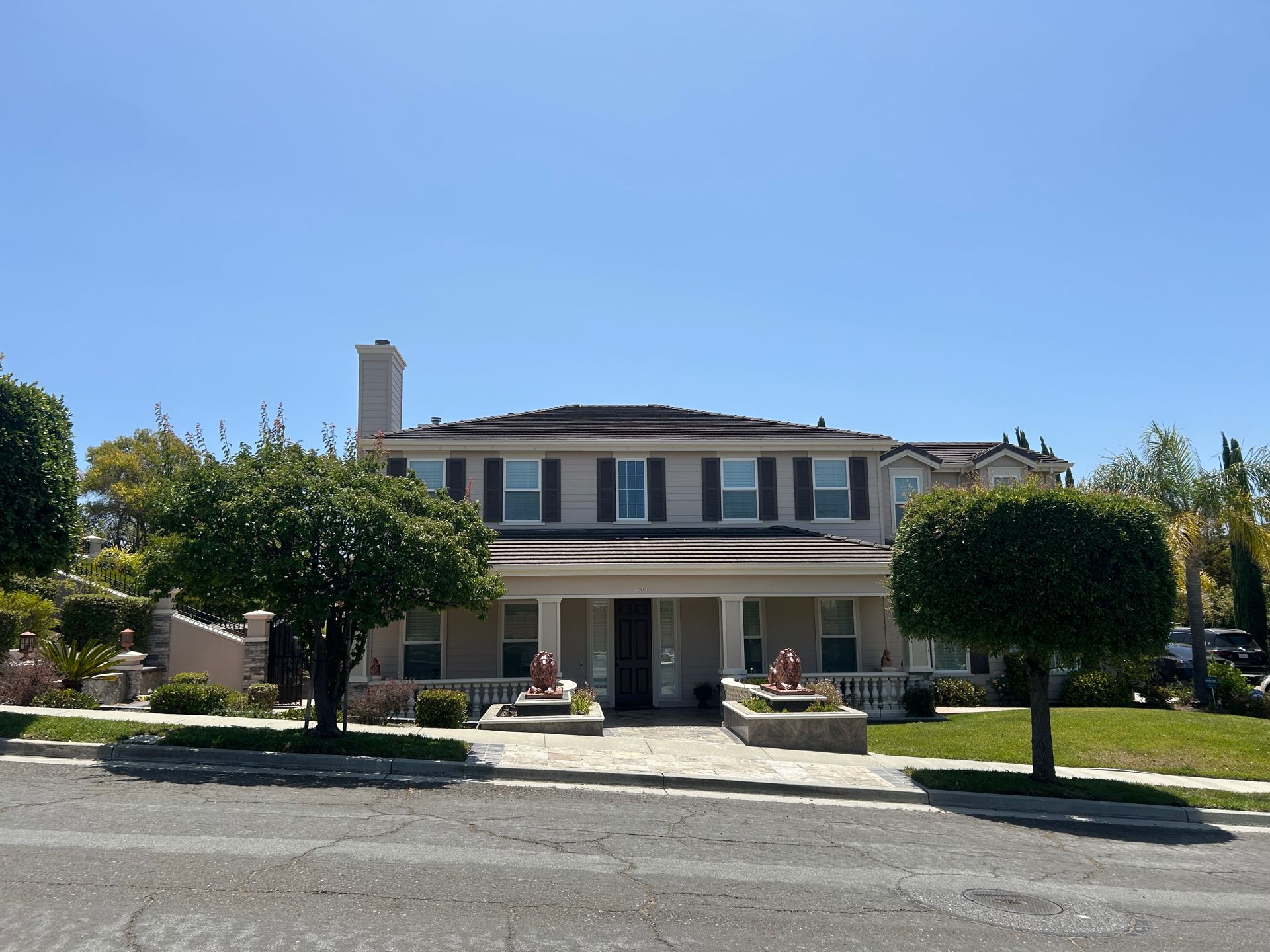 Two-story beige house with a covered porch, trees, and a clear blue sky.