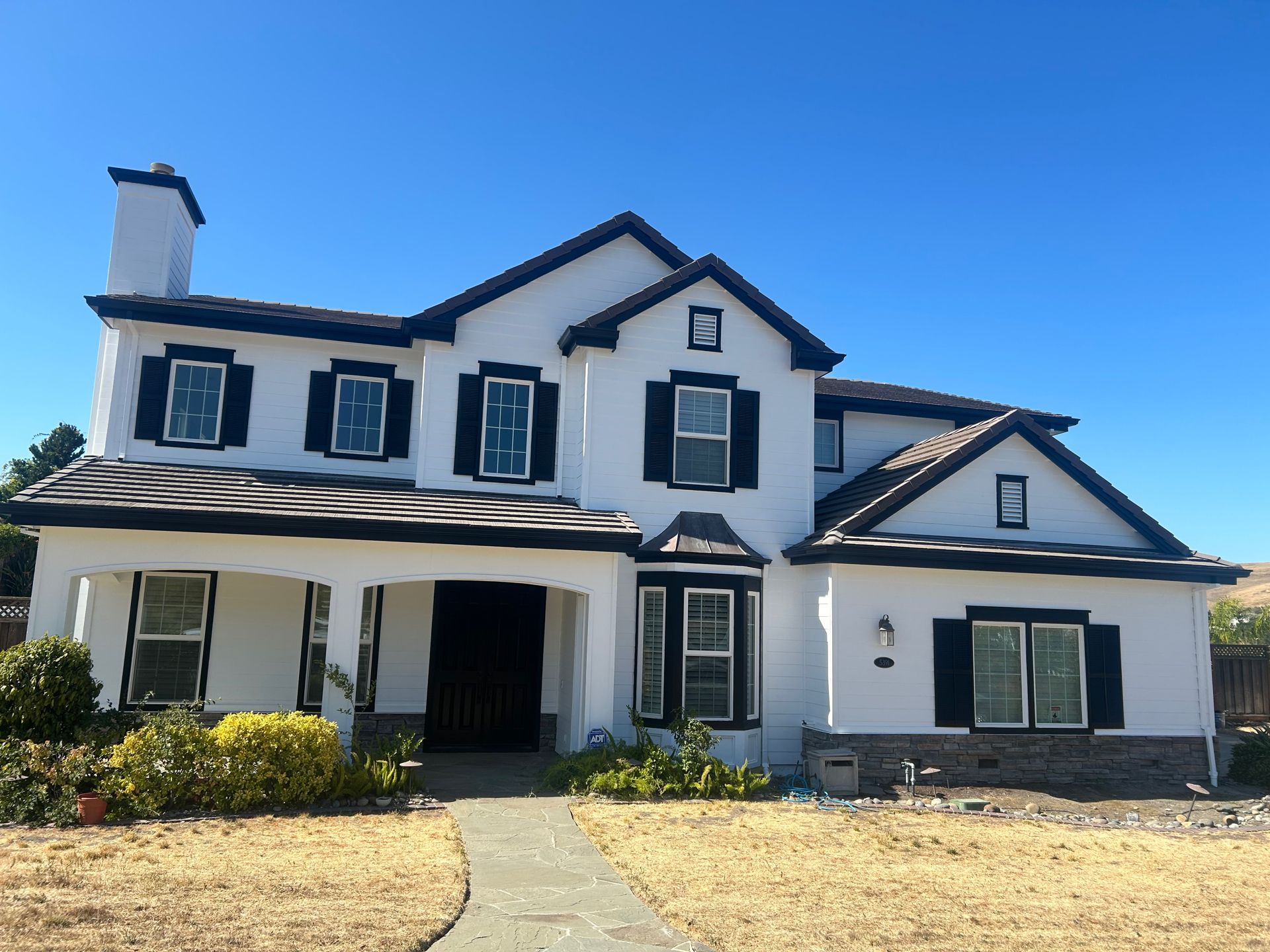White two-story house with black trim and shutters, blue sky backdrop.