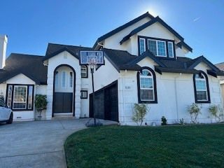White two-story house with black trim, basketball hoop, blue sky, and green lawn.