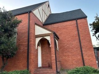 Brick building with a pointed arch entrance and gabled roof, tan trim, and dark shingles.