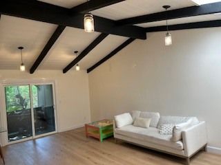 Living room with white walls, light wood floor, black beams, white sofa, and glass sliding door.